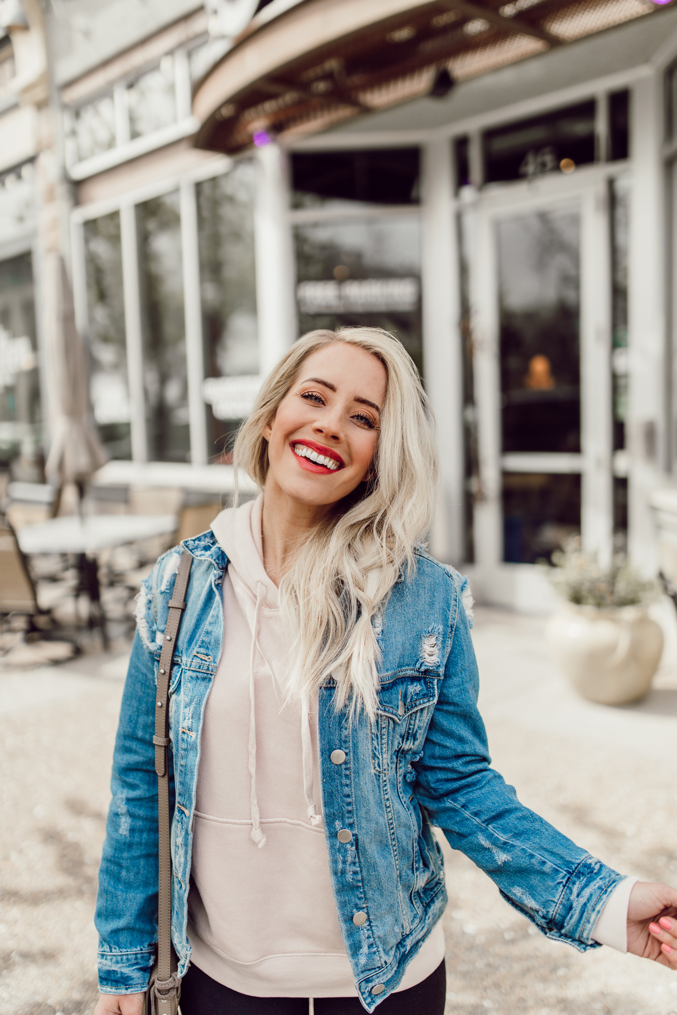 Fashion trendy casual young woman wearing a jean jacket and black leggings,  sitting in a public chair, searching for something inside of her purse in a  blurred background Stock Photo | Adobe
